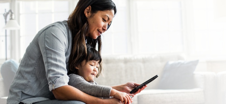 Woman sitting on the couch with her daughter at home using a smart phone powered by Spectrum Mobile.